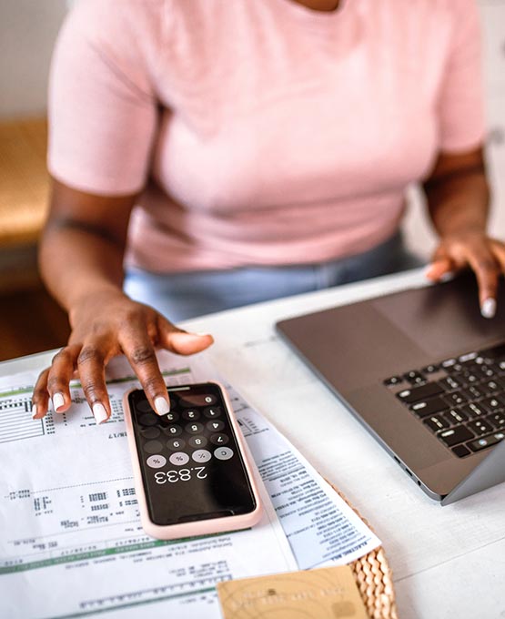Woman using a calculator on her phone and laptop.